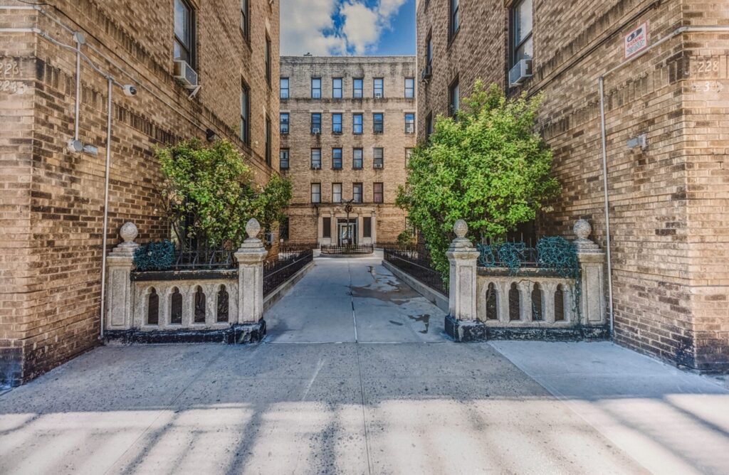 Entrance pathway to Naples Terrace apartments at 230 Naples Terrace, Bronx, NY 10463, featuring brick buildings and greenery